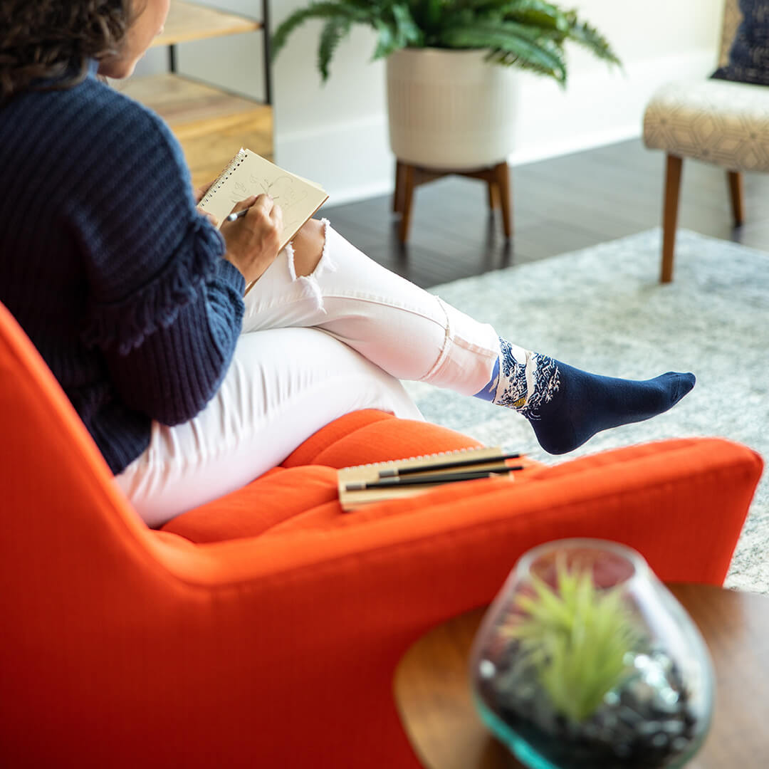 Person sitting on an orange chair in a living room, holding a notebook.