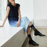 Woman sitting on a white bench wearing black dress shoes and socks with a design. thumbnail