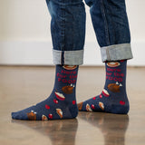 Person wearing blue socks with Thanksgiving-themed design and rolled-up jeans on a light wooden floor. thumbnail