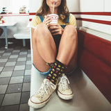 Person sitting in a diner wearing colorful socks and white sneakers, holding a drink.
