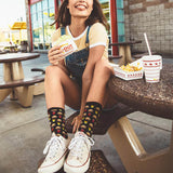 Person sitting at an outdoor dining table with fast food, wearing hamburger-patterned socks. thumbnail