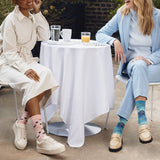 Two women sitting at a table outdoors, wearing colorful socks. thumbnail
