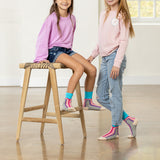 Two children wearing colorful socks and standing on a wooden floor.