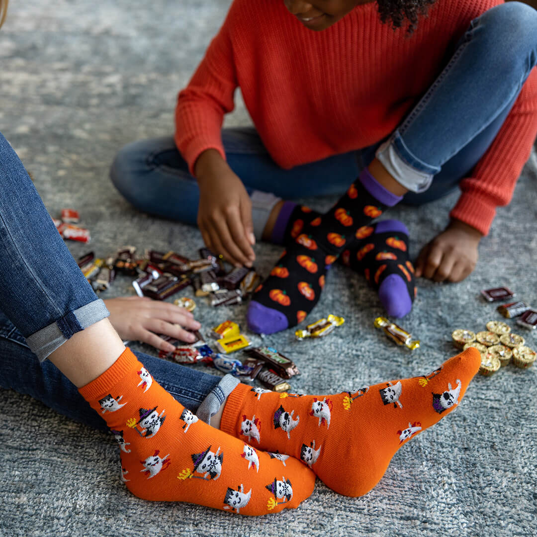 Two children sitting on the floor with Halloween-themed socks and candy.