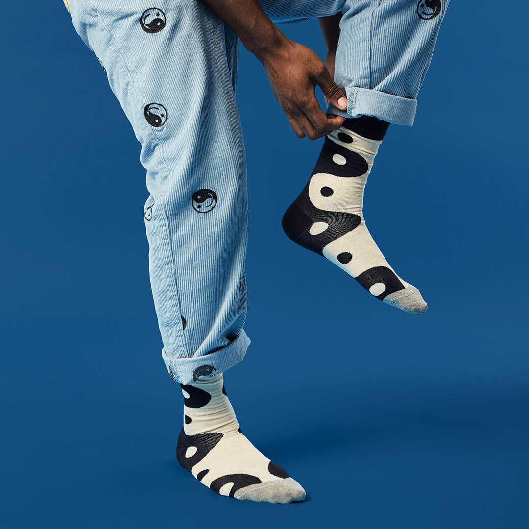 Person wearing light blue jeans and black and white yin yang socks against a blue background