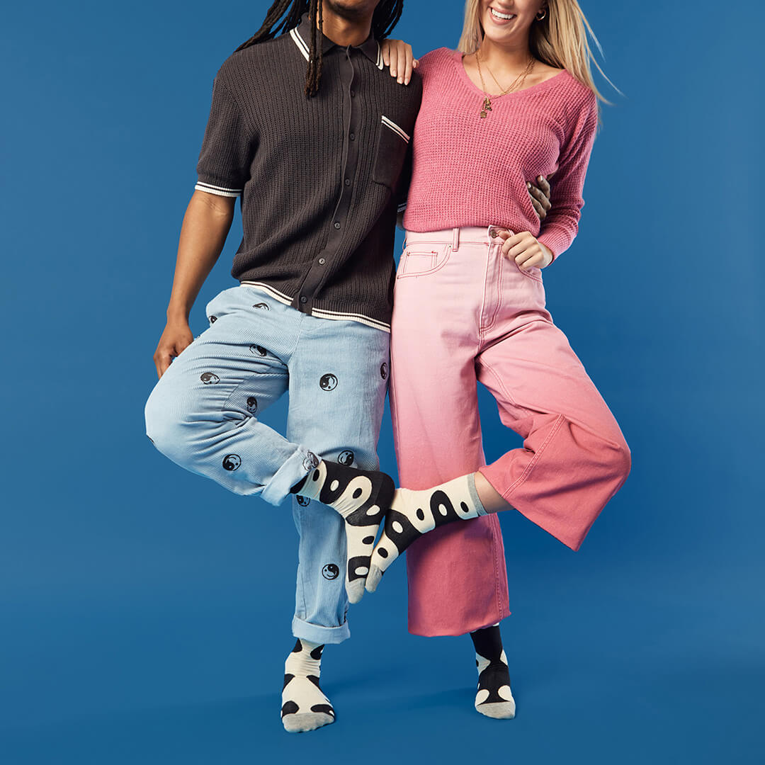Two people wearing matching black and white yin yang socks against a blue background