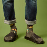 Person wearing sandals, rolled-up jeans, and patterned beer and pizza slice socks on a green background