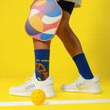 Person wearing colorful socks with 'The Dinker' designs, white sneakers, and a pickleball paddle on a yellow background. thumbnail