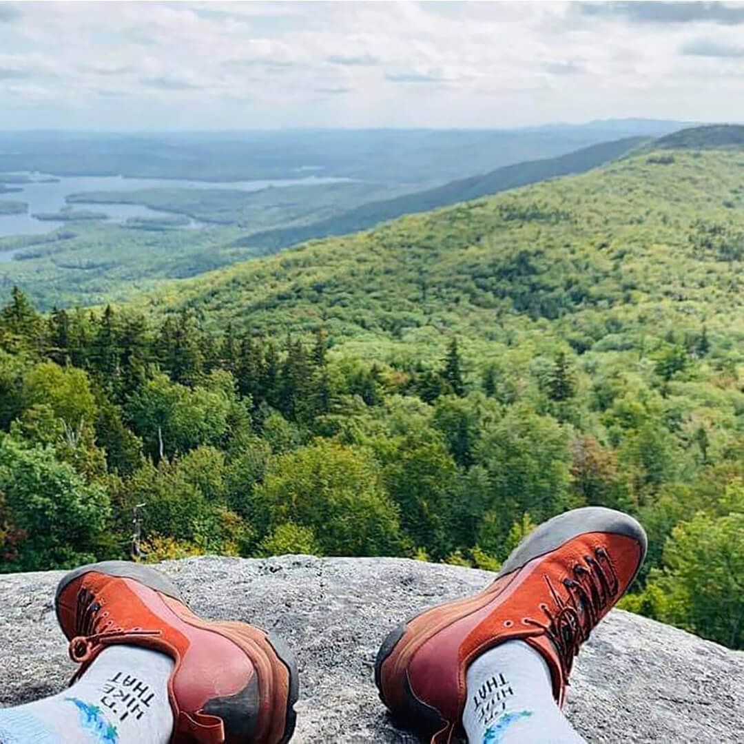 Red hiking boots on a rock with a scenic view of green hills and lakes.