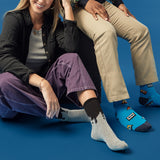 Two people sitting on a blue background wearing colorful socks with paint drip and cassette tape patterns.