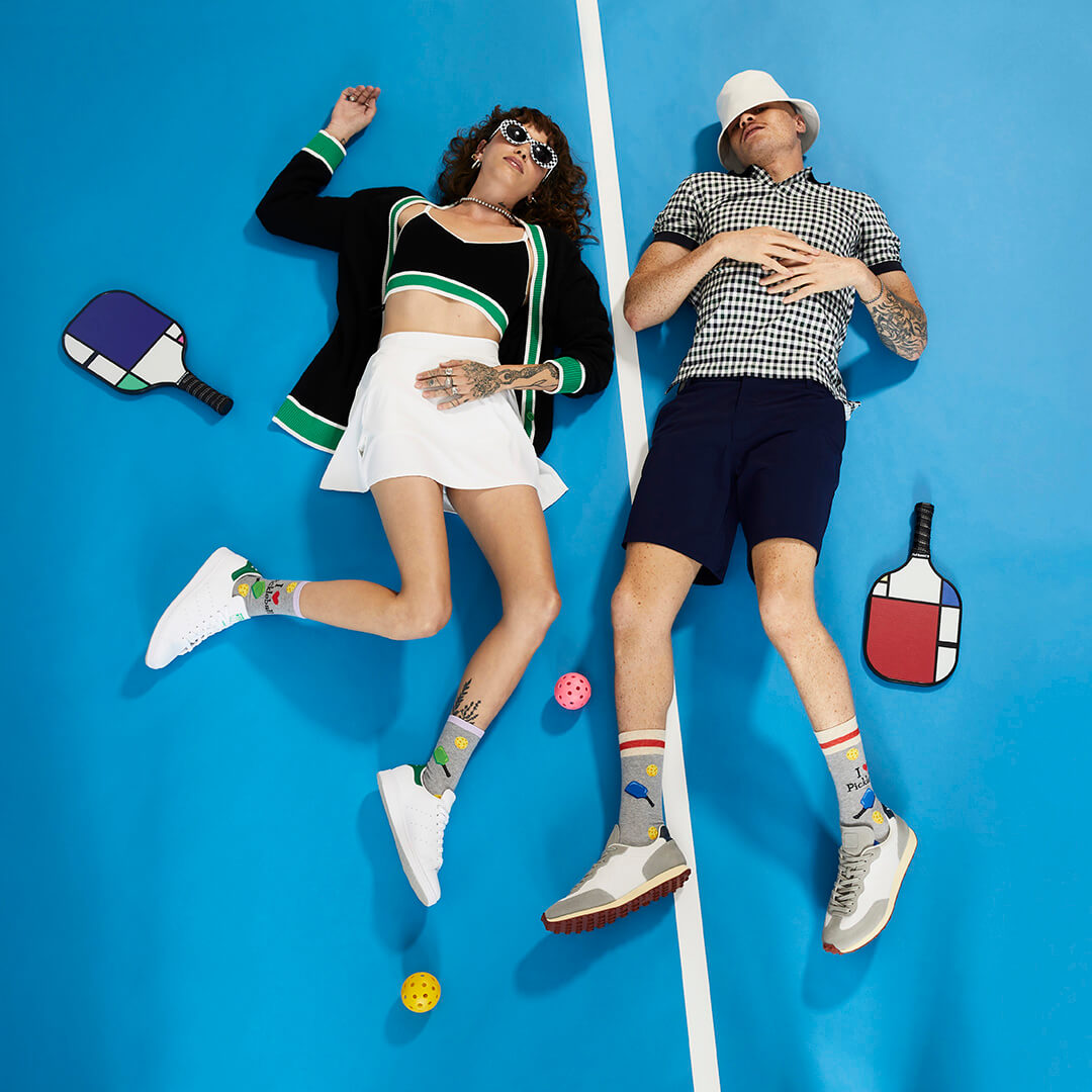 Two people lying on a blue surface with pickleball equipment around them.