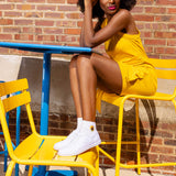 Woman in a yellow dress sitting on a yellow chair with a brick wall background thumbnail