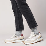 Person wearing white sneakers with red accents and gray jeans on a light gray background