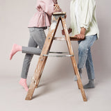 Two people using a wooden step ladder against a plain background