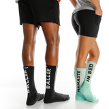 Two pairs of socks with text on them worn by people, one black with 'BALLER' and one green with 'NAMASTE IN BED'.