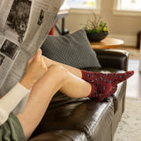 Woman sitting on a brown leather couch reading a newspaper, wearing red socks with black leopard patterns.