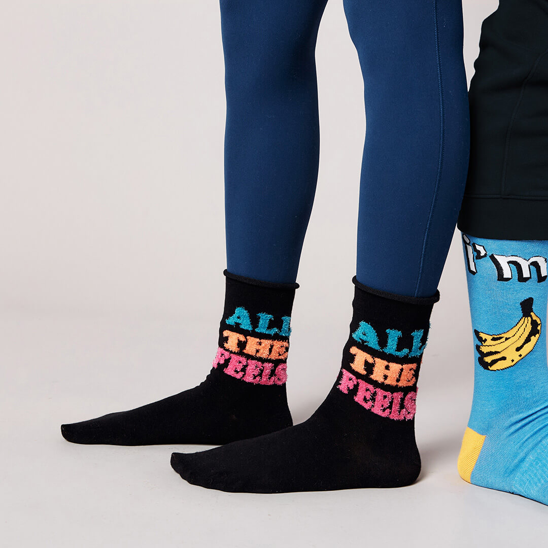 Black socks with colorful text and blue socks with banana design on a light gray background