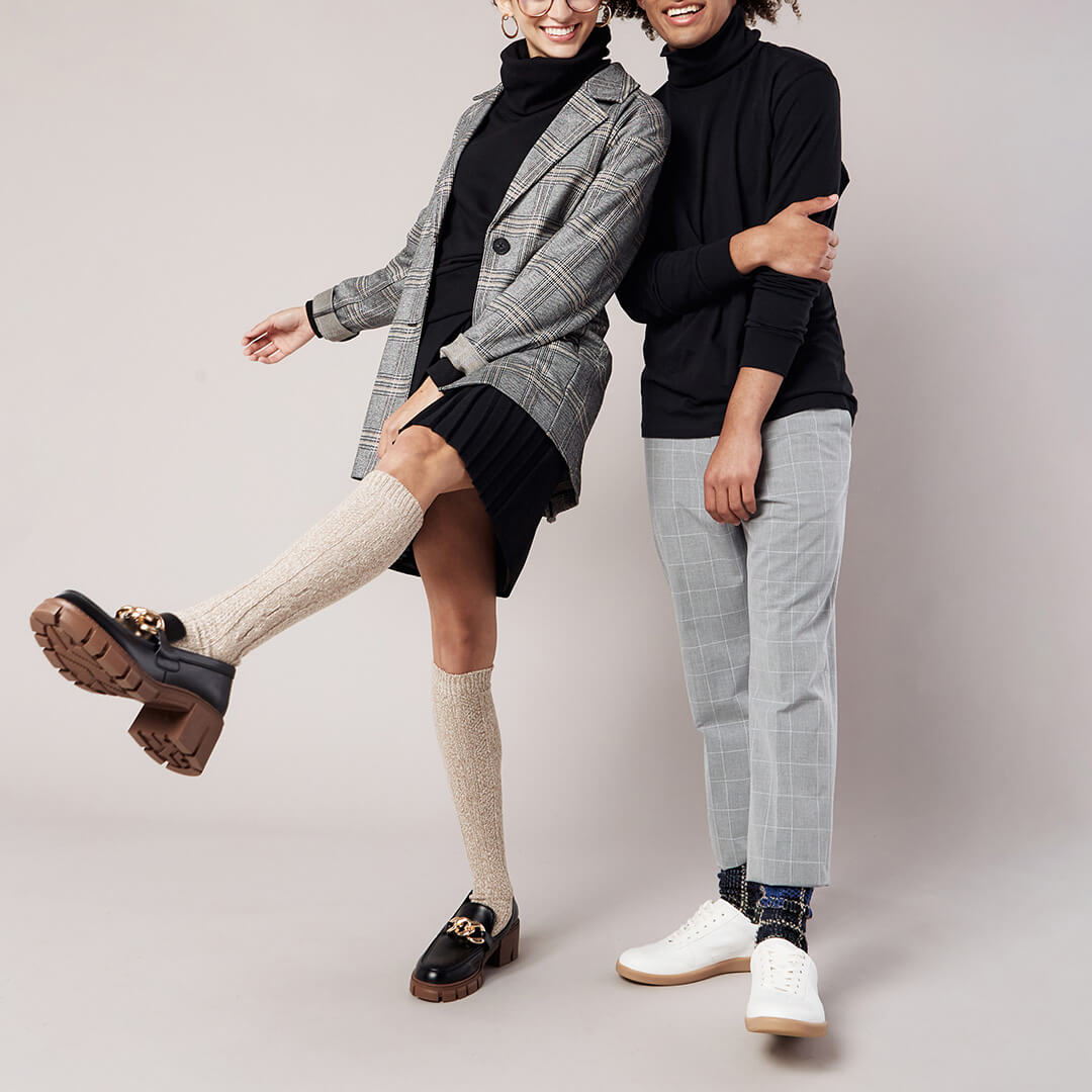 Two people posing together wearing stylish outfits with a plain background