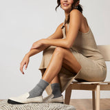 Woman sitting on a chair wearing a beige dress and gray socks with white shoes.