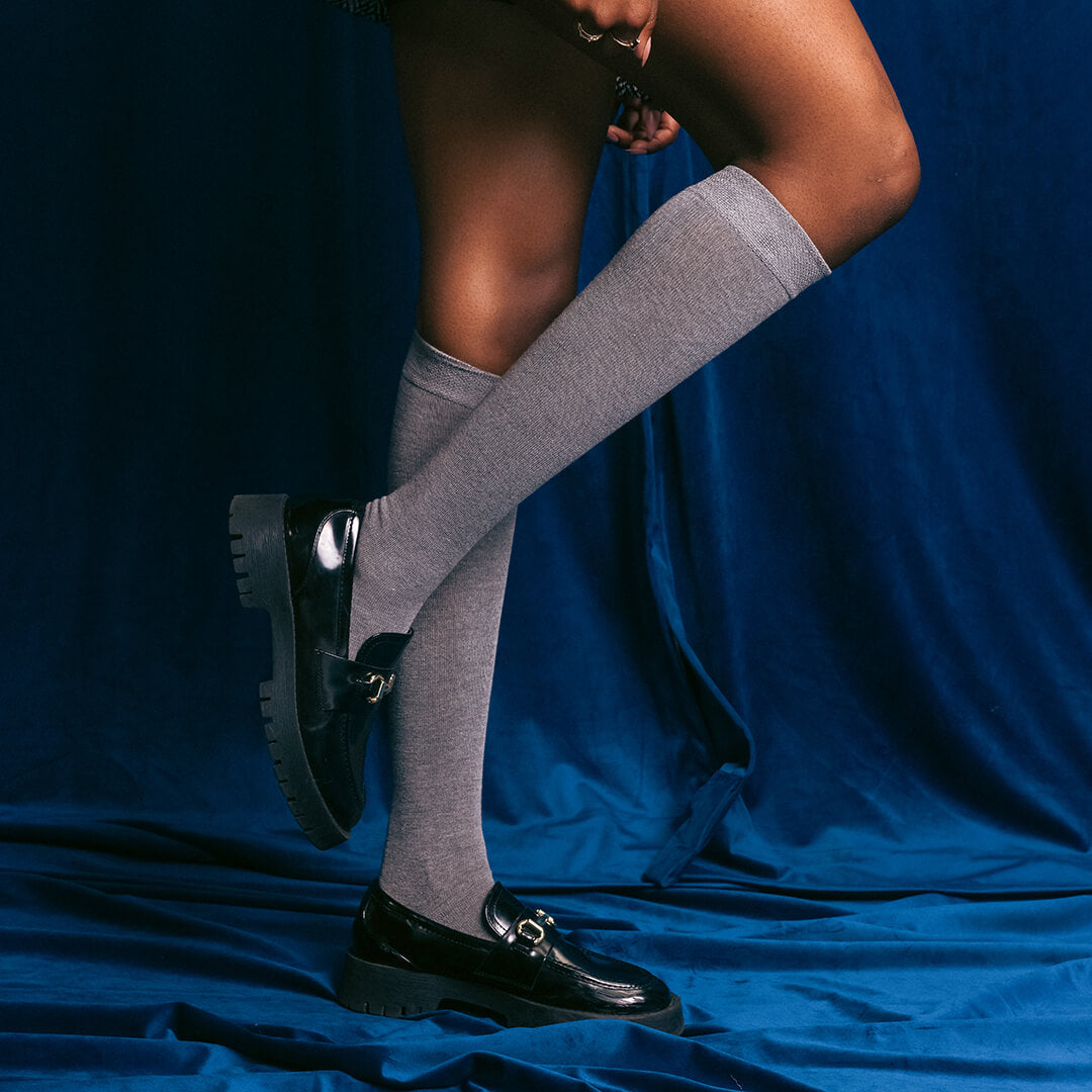 Gray knee-high socks worn with black shoes on a blue fabric background