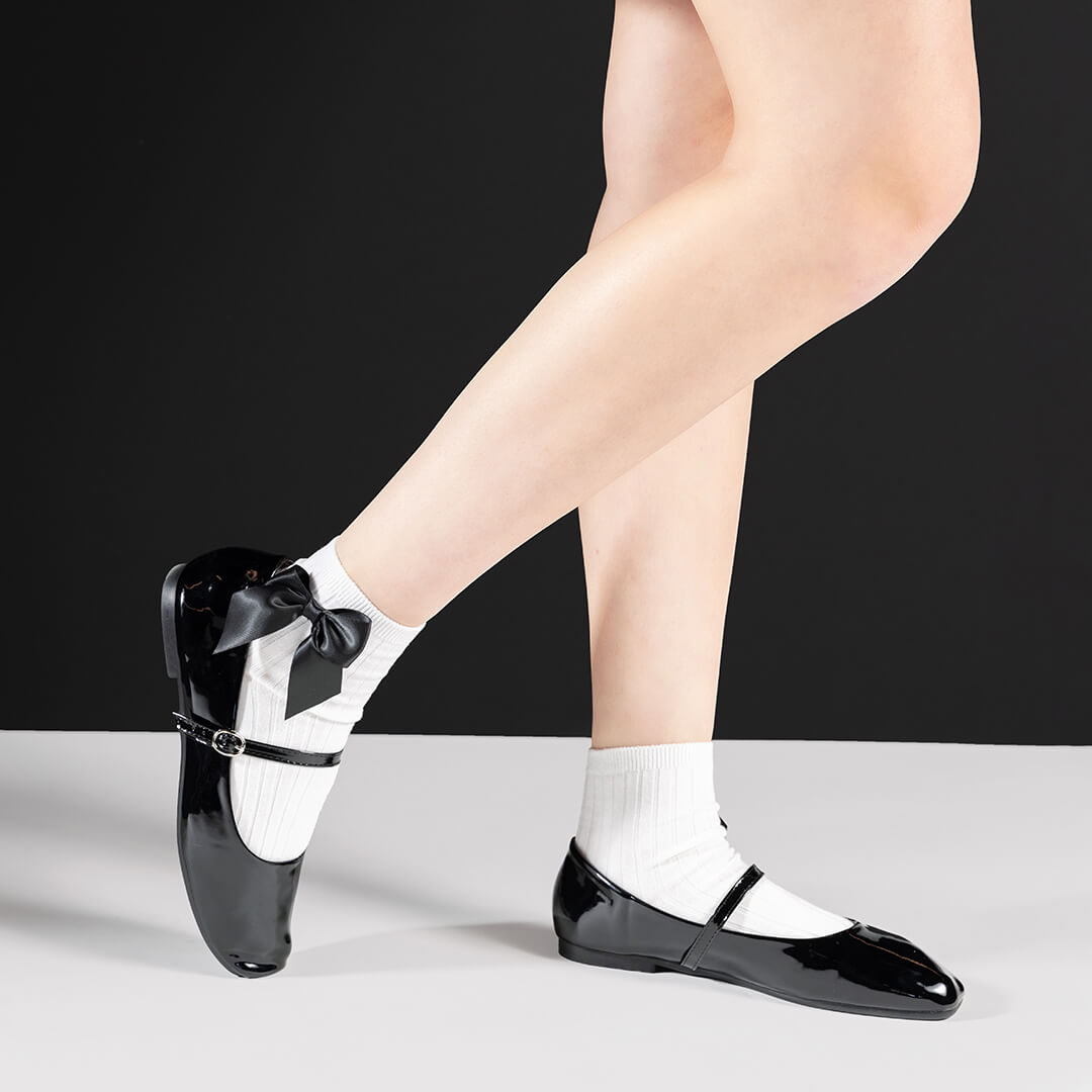 Black shoes with white ankle socks decorated with a giant black bow and black shoes on a white background.