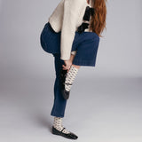 Person wearing blue jeans, a beige sweater, and patterned bow socks on a plain background thumbnail