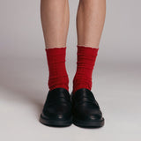 Red socks with white cuffs worn with black shoes on a neutral background thumbnail