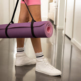 Person holding a purple yoga mat with white sneakers and pink shorts in a locker room.