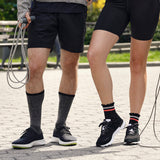 Two people wearing black athletic shoes and socks on a paved path. thumbnail