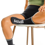 Person wearing black socks with 'BADASS' text, sitting on a chair. thumbnail