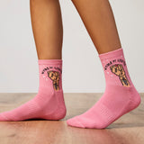 Pink socks with fist design and 'Women Unite' text worn by a person on a wooden floor. thumbnail